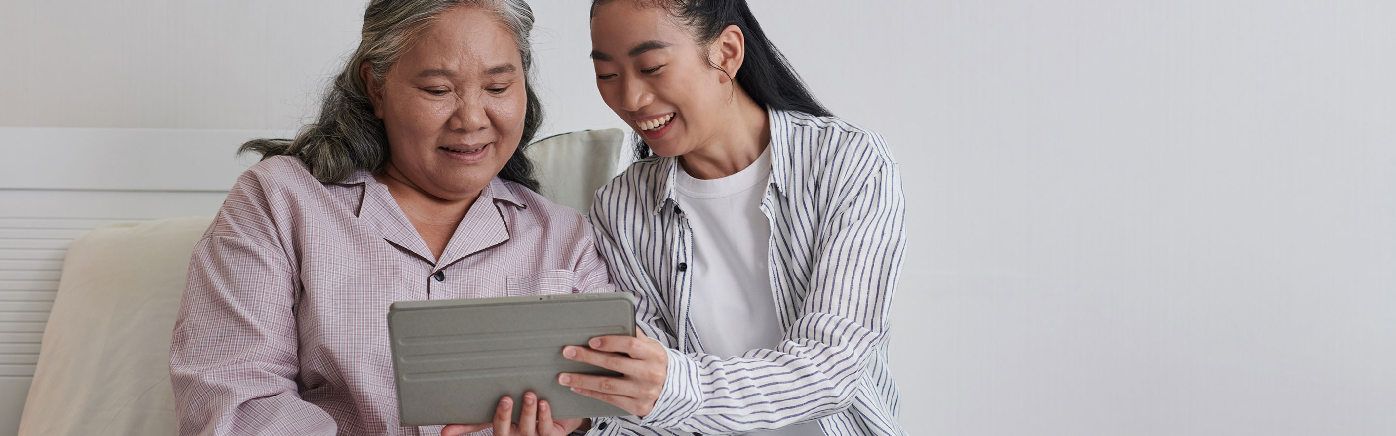 Mother and daughter sitting on bed using an ipad